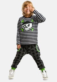 Camicetta a maniche lunghe a righe bianche e nere con grafica di teschio da pirata; pantaloni harem grigi con motivo a stelle; dettagli verdi; sneakers argentate.