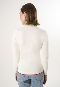 Witte lange mouwen trui met ribgebreide halslijn en manchetten, met een rode accenten aan de zoom, gecombineerd met blauwe high-waisted jeans.