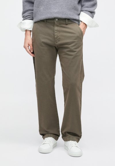 Βερμούδες από βαμβακερό μείγμα, ελαιοπράσινου χρώματος, με ίσια γραμμή, μπροστινές τσέπες, κλείσιμο με κουμπί και καθαρό τελείωμα, συνδυασμένες με λευκά αθλητικά παπούτσια.