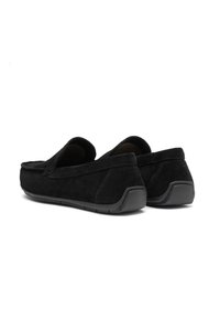 Mocassins en daim noir avec un bout arrondi, un design à enfiler et une semelle en caoutchouc. L'empeigne présente une texture lisse et des détails de couture minimaux.