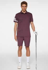 Morsevärinen golfpaita, jossa on kaulukset ja lyhyet hihat, sekä valkoinen korostusraita. Paita on yhdistetty samaan morseväriseen shortsipariin ja golfmailaan.