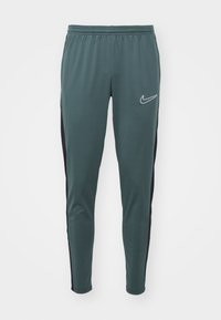 Groene sportbroek van gladde stof, met een contrasterend zwart zijpaneel en een klein wit Nike-logo aan de voorkant.