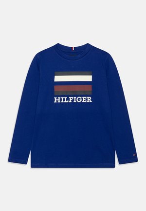 Blå langærmet skjorte med sorte, hvide og mørkerøde vandrette striber og ordet "HILFIGER" trykt under striberne.