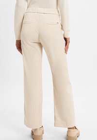 Beige Cord-Pantalons mit entspanntem Schnitt, elastischem Bund und zwei Gesäßtaschen. Der Stoff hat eine gerippte Textur und eine glatte Oberfläche.
