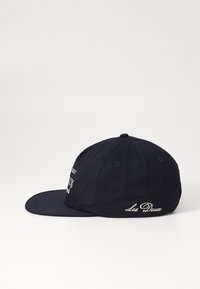 Navy blue baseball cap made of cotton. Features a curved brim, embroidered lettering on the front and back, and a structured crown.