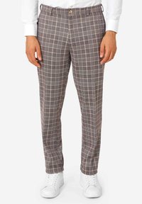 Pantalones de cuadro en tonos marrón y gris, con un ajuste entallado, cierre de botón, trabillas para cinturón y bolsillos laterales. Combinados con zapatillas blancas.
