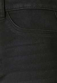 Tejido de mezclilla negra con una textura lisa, que presenta un bolsillo frontal y sutiles detalles de costura a lo largo de los bordes.