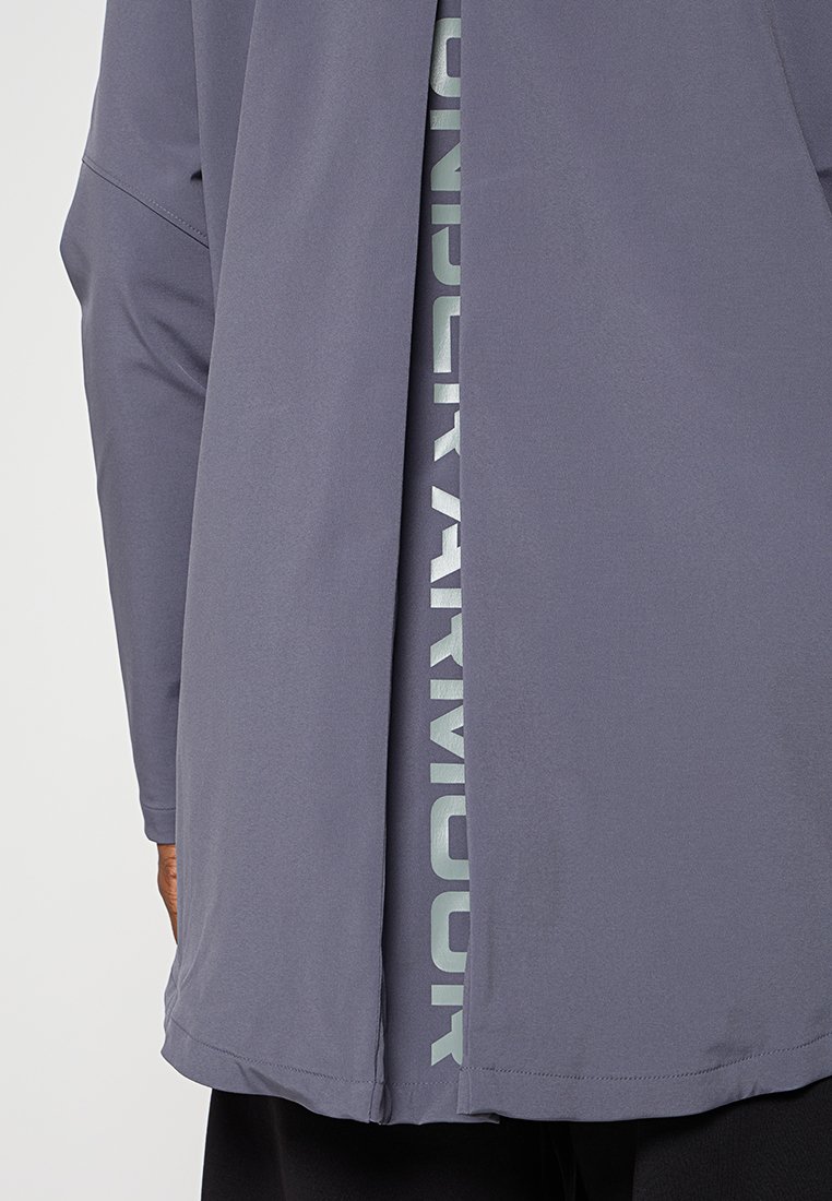 Vêtement d'extérieur à manches longues, gris clair avec un dos fendu, présentant du texte vert visible en dessous. Tissu doux avec une texture lisse.