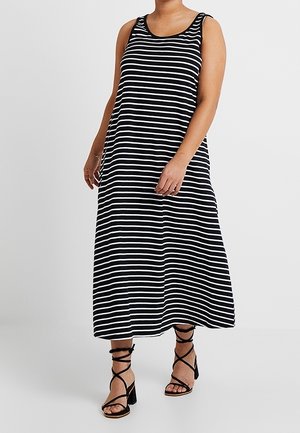 Femme portant une robe midi sans manches à rayures horizontales noires et blanches avec des sandales noires à talon bloc et lacets.
