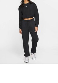 Svart kortärmad sweatshirt med dragsko nederkant, med en vit Nike-logga, kombinerad med löst sittande svarta mjukisbyxor och silverfärgade sneakers.