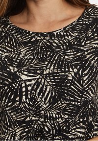 Černobílý top s designem listů palmy. Hladká textura s kulatým výstřihem; látka má jemný lesk.