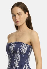 Abito senza spalline di colore blu navy con corpetto arricciato, motivo floreale bianco e un tessuto morbido e testurizzato. Presenta un dettaglio con cordoncino al collo.