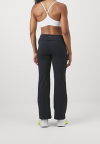 Czarna odzież sportowa z rozszerzanymi nogawkami, zestawiona z białym biustonoszem sportowym. Całość charakteryzuje się gładką strukturą i dopasowanym krojem.