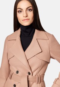 Płaszcz z mieszanki wełny w odcieniu różu z podwójnym zapięciem, dużymi klapami i pasującym paskiem. Miękka tekstura i ciemne akcenty guzików.