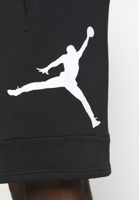 Černé šortky s hladkým povrchem, na levé noze mají velkou bílou siluetu skákající postavy. Lem je zakončen pruhem.