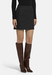 Une mini-jupe en laine grise associée à des bottes marron en cuir foulonné avec embosse crocodile, hauteur genou et à bouts pointus. Un haut à manches longues noir côtelé.