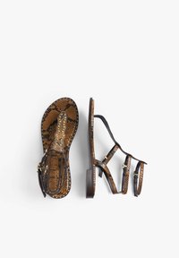 Sandalias de serpiente marrón con múltiples correas de cuero negro y tachuelas doradas. El diseño cuenta con una suela plana y una correa ajustable en el tobillo.