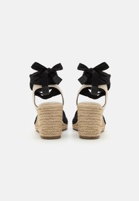 Black espadrille wedges featuring a woven jute heel, fabric straps tied at the ankle, and a contrasting tan base.