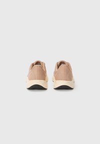 Beige athletic shoes with a textured upper, padded collar, and contrasting cream midsole, featuring a black outsole for grip.