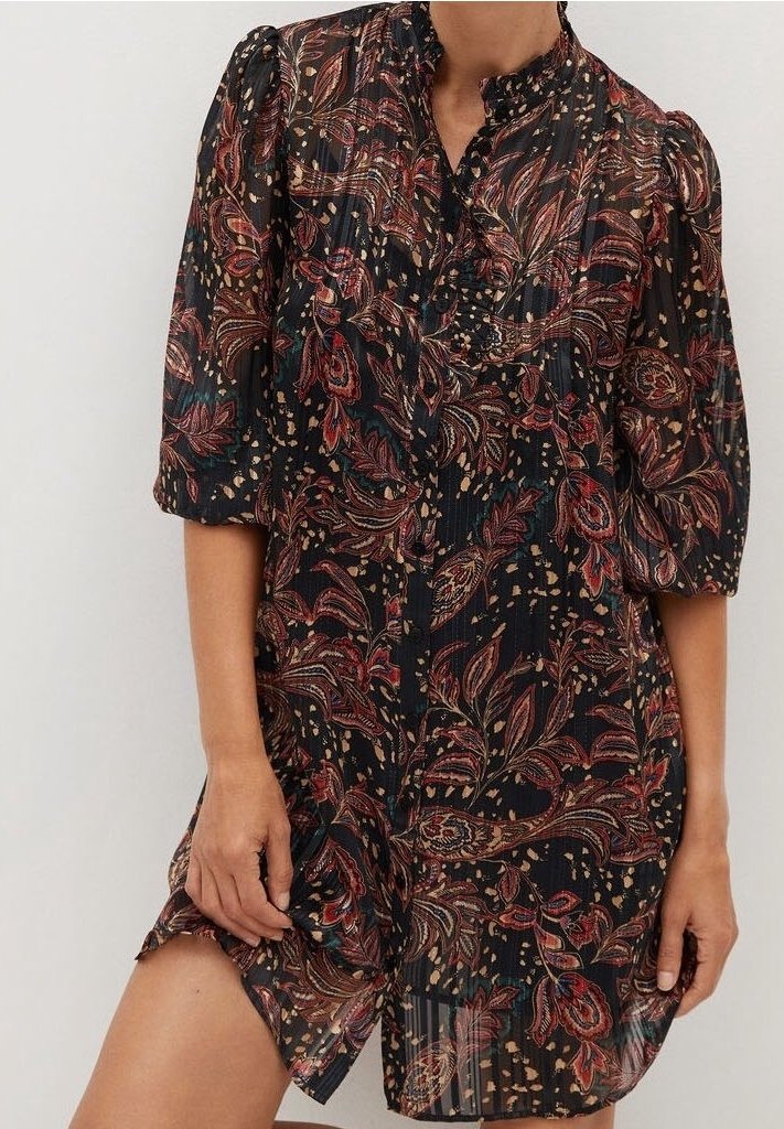 Vestido negro transparente con coloridos patrones florales y de paisley, mangas abullonadas y un cuello alto. Presenta detalles de botones y plisados.