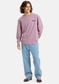 Langærmet lavendel skjorte med et lille logo på brystet, parret med lyse denim jeans og mørke sneakers med hvide snørebånd.