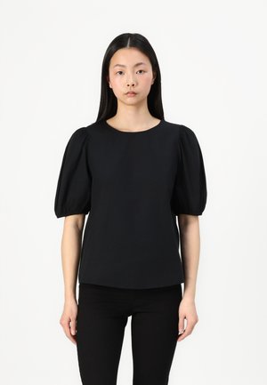 Haut noir à manches courtes bouffantes et col rond. Fabriqué en tissu lisse avec une coupe structurée. Associé à un pantalon noir ajusté.