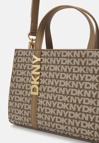 Torebka DKNY w kolorze brązowym z kremowym wzorem logo, z akcentem w kolorze złotym i odpinanym paskiem dla większej wszechstronności. Gładki materiał syntetyczny.