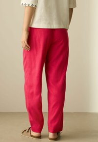 Pantalones de lino rosas con corte recto, con costuras laterales y un ajuste relajado, combinados con zapatos marrones sin cordones y una blusa de manga corta.