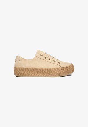Beiger Canvas-Low-Top-Sneaker mit dicker, gewebter Jutesohle und beigen Schnürsenkeln, seitlich auf weißem Hintergrund gezeigt.