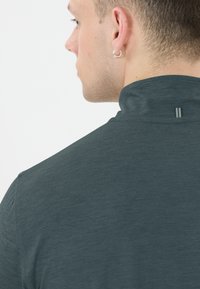Donkerblauwe, kortiemouwen shirt met een hoge kraag. Zachte, textuurstof met een klein logo detail op de achterkant van de kraag. Minimalistisch ontwerp.