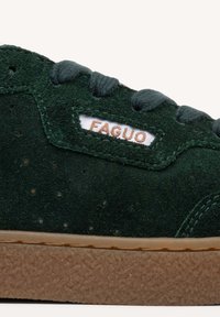 Baskets en suede vert présentant un dessus texturé, des lacets ronds et une semelle en caoutchouc marron. Une petite étiquette blanche avec "FAGUO" est cousue sur le côté.