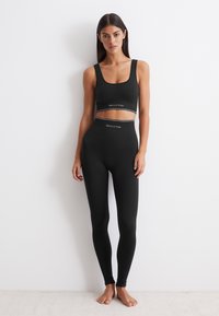 Černá žebrovaná sportovní podprsenka a legíny s vysokým pasem, které se vyznačují přiléhavým střihom, kontrastním elastickým pásem v pase a jemným logem.