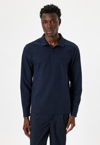 Laivastonsininen pitkähiha polo-pait, jossa on teksturoitu kangas, ribba collar ja kolmipaikkainen napitus. Yhdistetty tummien housujen kanssa.