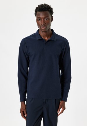 Polo de manga larga en color navy, con un tejido texturizado, cuello acanalado y tapeta de tres botones. Combinado con pantalones oscuros a juego.