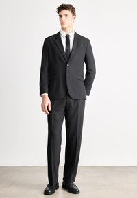 Czarny garnitur z jednym guzikiem, dwie przednie kieszenie, dopasowany krój, zestawiony z białą koszulą i czarnym krawatem, noszony z czarnymi butami.