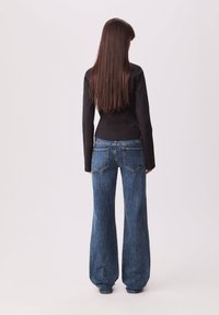 Blazer noir ajusté, taille haute, jeans évasés bleu clair avec texture denim, poches arrière visibles et détails de couture contrastants.