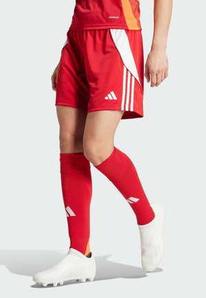 Rode sportieve shorts met witte accenten, gecombineerd met rode sokken en witte voetbalschoenen. Materiaal lijkt ademend; de shorts hebben drie witte strepen.