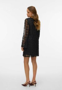 Černé krajkové šaty s dlouhými rukávy, poloprůhlednou strukturou, vroubkovaným lemem a květinovými vzory. Kombinované s vínově červenými lodičkami na podpatku.