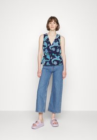 Top peplum floral em azul-marinho com padrões paisley em verde e azul, combinado com jeans de pernas largas em azul-claro e sandálias de plataforma em lavanda.