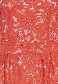 Tissu en dentelle rouge avec des motifs floraux présentant de grandes fleurs et des feuilles, ainsi que des zones transparentes entre les broderies détaillées.