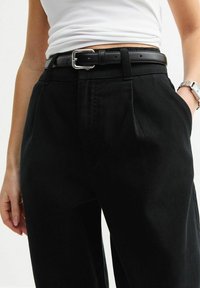 Svarta högmidjade byxor i texturerat tyg med veckad front, sidofickor och ett svart läderbälte med silverfäste.