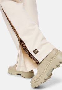 Beige sweatpants with leopard print accents and side slits, paired with chunky beige sneakers featuring a textured sole.