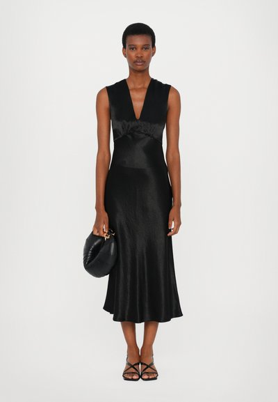 Svart satin midi-klänning med djup V-ringning, figurnära överdel med rynkdetalj och utsvängd nederdel. Accessoriserad med en rund svart kuvertväska.