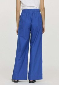 Pantalons larges bleu avec une taille élastique, confectionnés en tissu lisse. Ils présentent une coupe ample, atteignant le sol, avec une couleur unie.