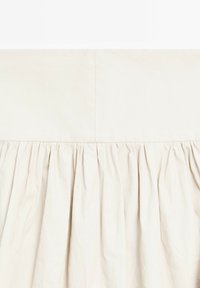 Jasno beżowa spódnica z gładkim, płaskim pasem. Materiał ma miękką teksturę, z zebranymi fałdami na dole, co dodaje objętości.
