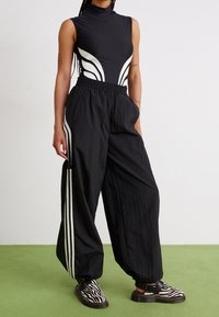 Bodysuit negro con acentos de diseño en blanco, combinado con pantalones negros ajustados que presentan rayas laterales blancas y un acabado texturizado, usados con zapatos de rayas.