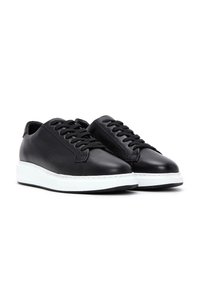 Sneakers in pelle nera con punte rotonde, lacci bianchi piatti, suola in gomma bianca e design minimalista. Texture liscia senza motivi visibili.