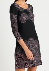 Svart klänning med rundad halsringning, trekvartslånga ärmar och intrikata rosa blommönster i spets vid fållen och ärmsluten.