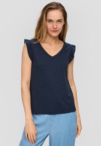 Granatowa bezrękawnikowa bluzka z dekoltem w serek i falbankami na ramionach, wykonana z miękkiej bawełny, w połączeniu z jasnoniebieskimi dżinsami.