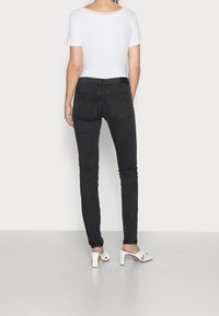 Musta kapealahkeiset farkut, joissa on keskikorkea vyötärö ja kaksi takataskua, yhdistetty valkoiseen lyhythihaiseen toppiin, jossa on aaltoileva pääntie, sekä korkokenkiin.